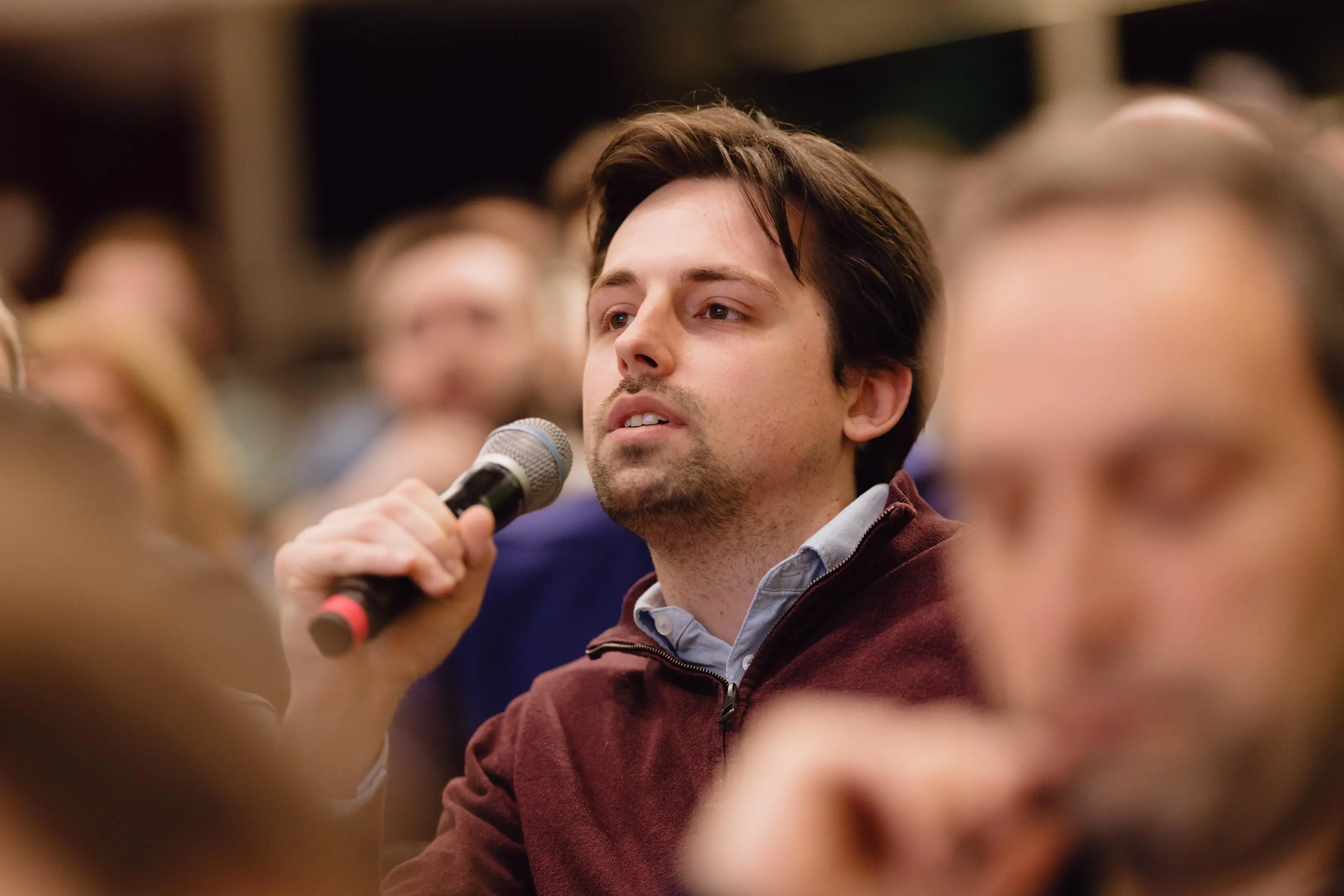 Tim Damen sitting in crowd holding a microphone